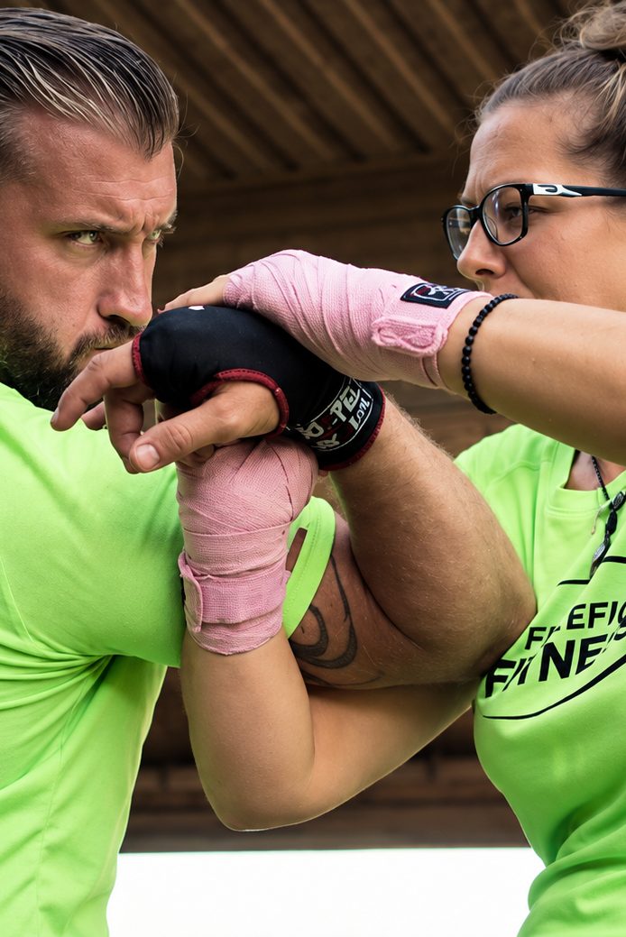 Trainer und Teilnehmerin üben einen Handgelenkhebel im Selbstverteidigungstraining