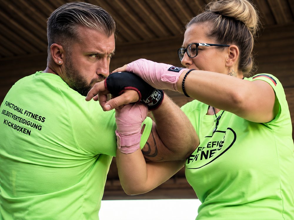 Trainer und Teilnehmerin üben einen Handgelenkhebel im Selbstverteidigungstraining